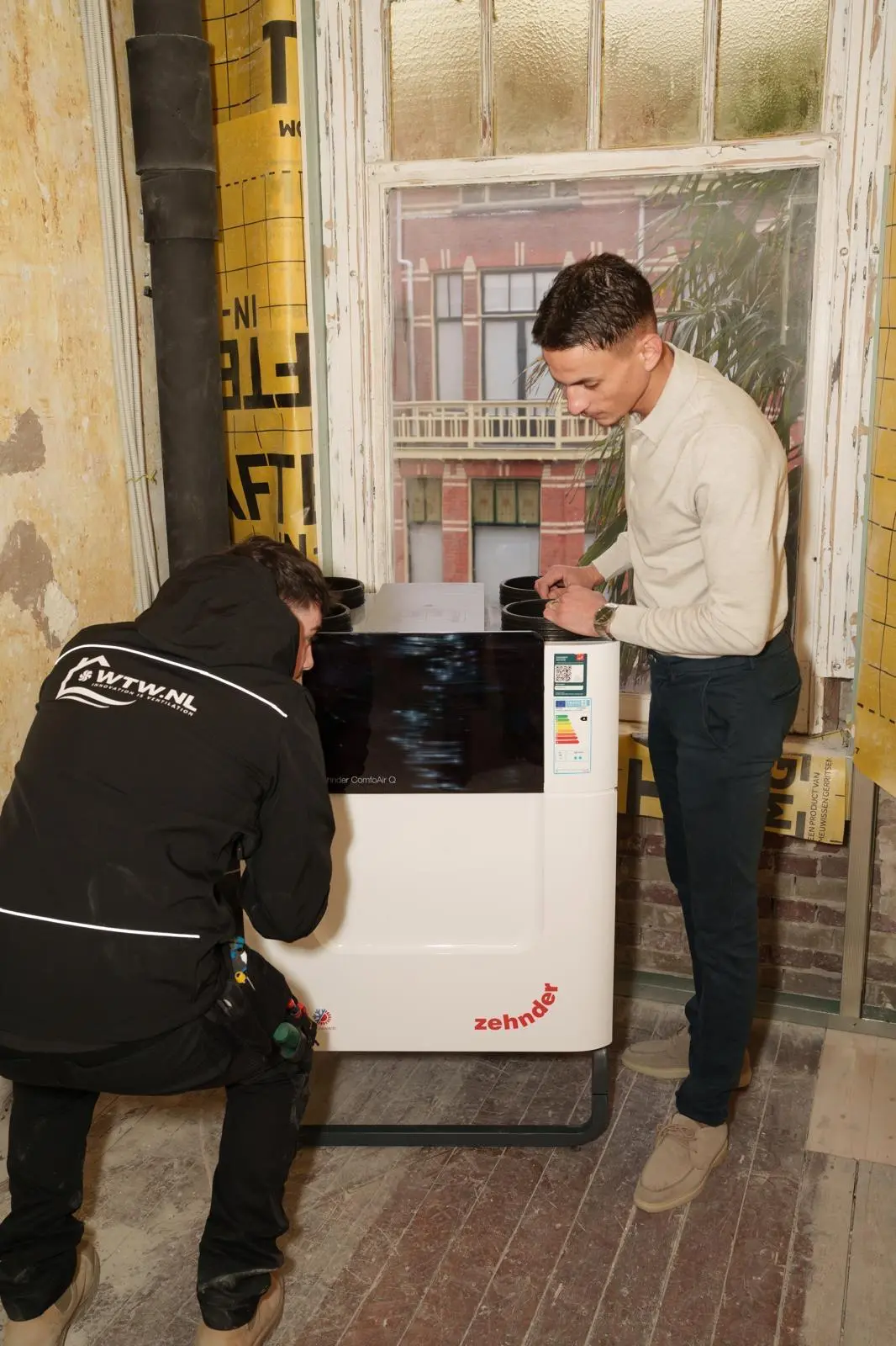 Moncif Hakmaoui, oprichter WTW.nl, gehurkt naast een Zehnder ComfoAir Q WTW-unit